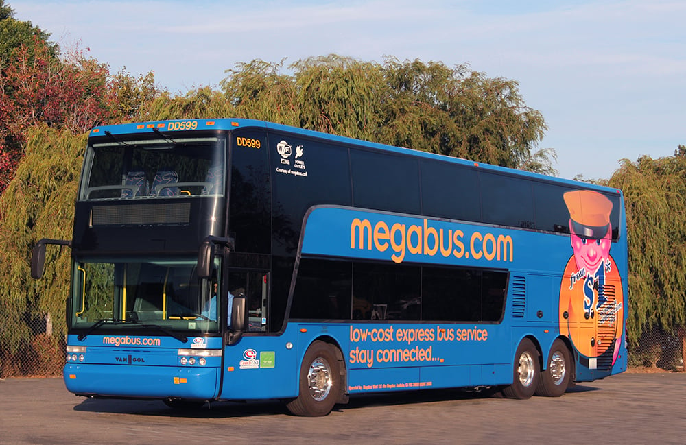 Photo of a Megabus on a sunny day, parked in a wooded area.
