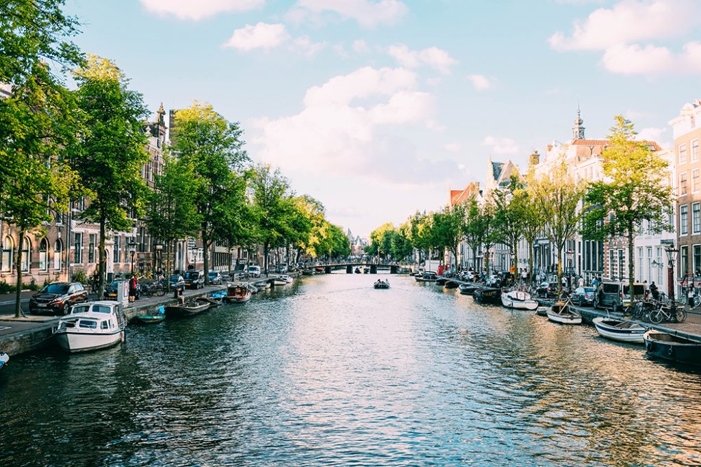 Picture of a canal in Amsterdam on a sunny day lined with small boats.