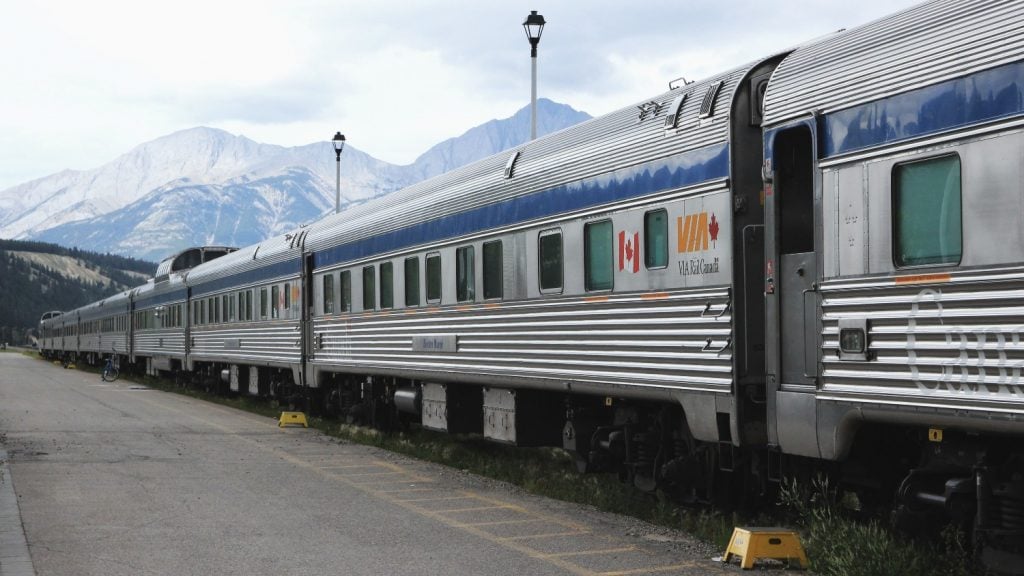 A VIA Rail train pulls into the station with mountains in the background