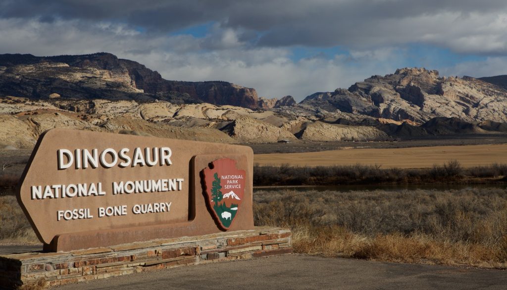 A National Parks Service sign points towards the Dinosaur National Monument amid a rocky Colorado landscape