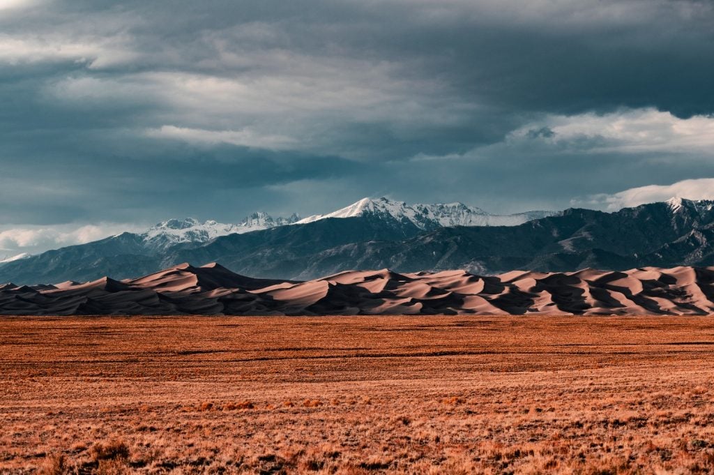 The dunes of Great Sand Dunes National Park appear before snowy mountain peaks