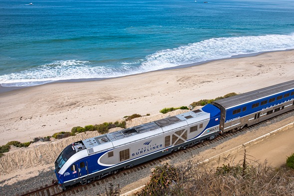 An Amtrak Pacific Surfliner alongside a sandy beach and the Pacific Ocean