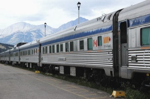 A VIA Rail train pulls into the station with mountains in the background