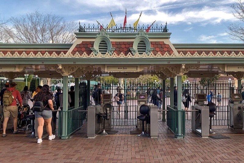 The main entrance gate and turnstiles of Disneyland in Anaheim on a sunny day, with flags flying over the canopy