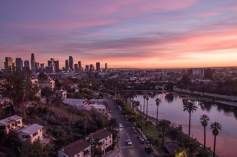 The downtown Los Angeles skyline at golden hour seen across Echo Park Lake, with palm trees along the shore