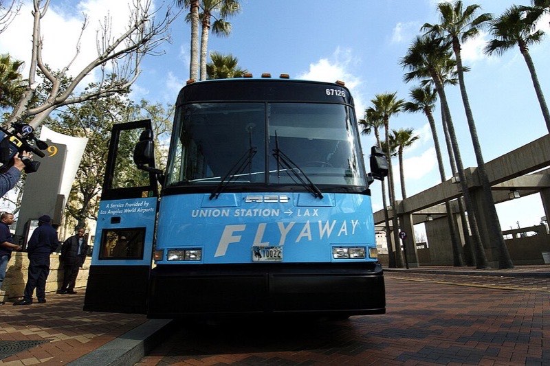 A bright blue LAX FlyAway coach with "Union Station to LAX" on its destination band, parked at a palm-lined Union Station bus stop