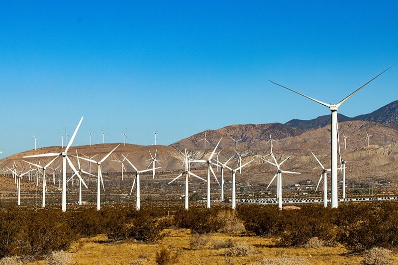 White wind turbines of the San Gorgonio Pass wind farm against desert mountains and a deep blue sky on the approach to Palm Springs